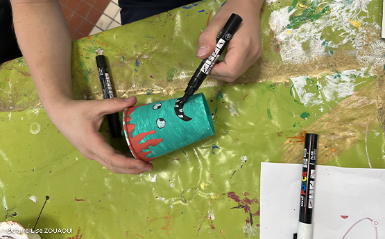 mains de garçons qui colorie et dessine sur un gobelet en carton polyèdre seynod annecy