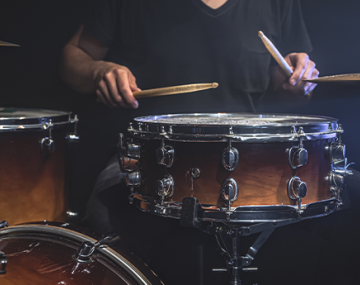 musicien en t-shirt noir joue de la batterie avec des baguettes sur scène